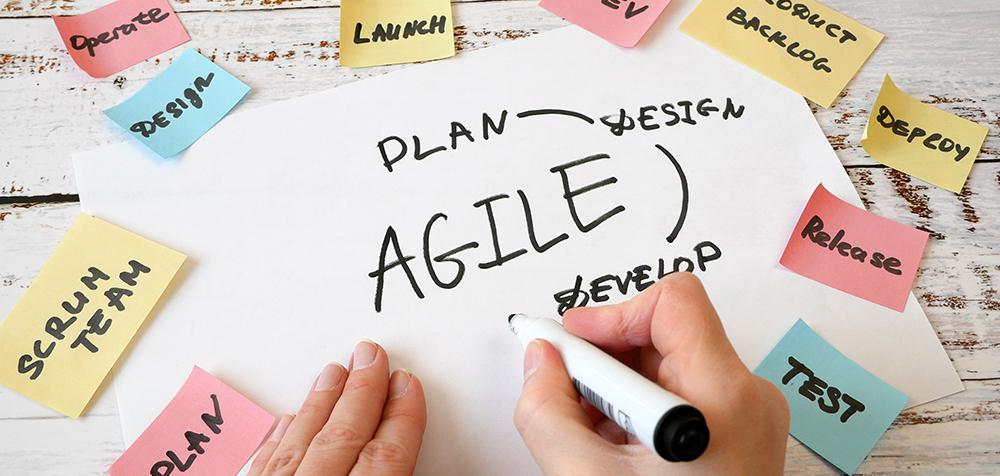 A person with hands only visible, writes on a progress board filled with post-its with different stages of the iterative design process written on them